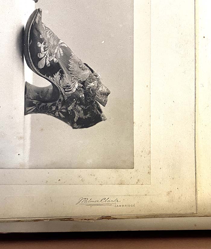 Detail of a page of a scrapbook showing a black and white photograph of a shoe and an imprint of the photographers Messrs. Palmer-Clarke.