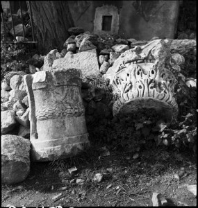 Black and white photo of ancient capitals heaped among ruins 