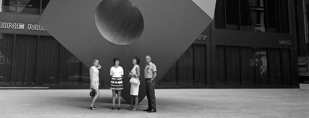 People standing in front of public art work in shape of large cube