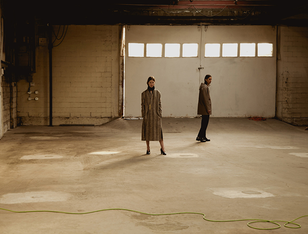 Two models stand in empty warehouse all in khaki tones