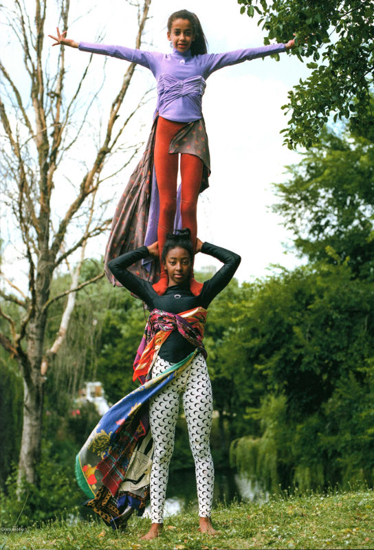 Young woman stands on shoulders of 2nd young woman. Both wear knitwear by designer Marine Serre.